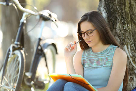 Single student wearing eyeglasses memorizing notes sitting in a parkの写真素材