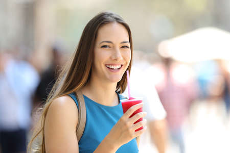 Happy woman holding a slush and looking at you in the streetの写真素材
