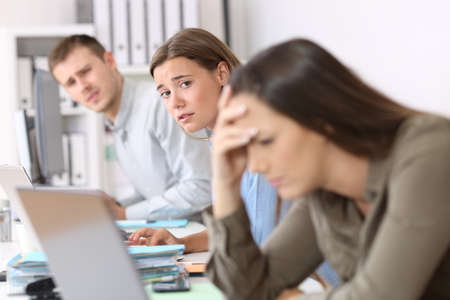Sad workers looking at a frustrated colleague who is reading bad news on line at officeの写真素材