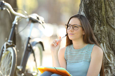 Single student thinking and looking at side sitting in a parkの写真素材