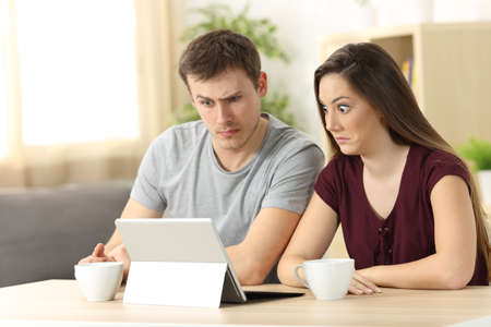 Confused couple receiving on line news sitting in a desk at homeの写真素材