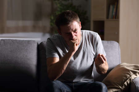 Front view portrait of a single furious man at home in the dark sitting on a sofa at homeの写真素材