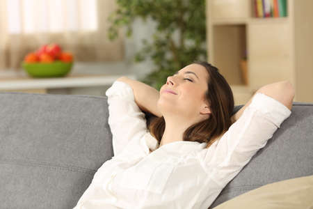 Happy homeowner relaxing alone sitting on a couch at homeの写真素材