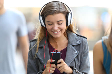 Front view portrait of a happy girl listening to music wearing headphones and walking on the streetの写真素材