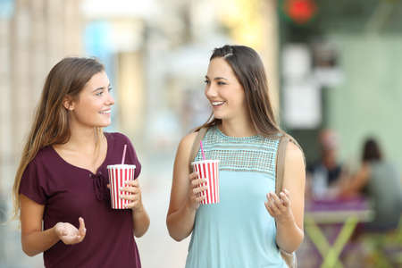 Front view of two friends walking towards camera and holding refreshments in the streetの写真素材