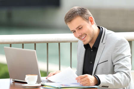 Happy executive reading documents sitting in a coffee shopの写真素材