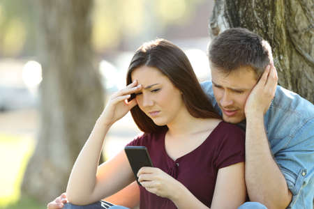 Worried couple using a smart phone to view on line content outside in a parkの写真素材
