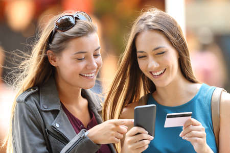 Two happy friends buying on line with credit card and smart phone on the streetの写真素材