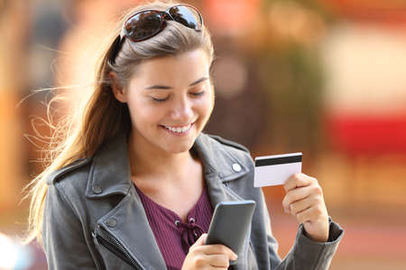 Portrait of a happy shopper buying on line with a smart phone and credit card on the streetの写真素材