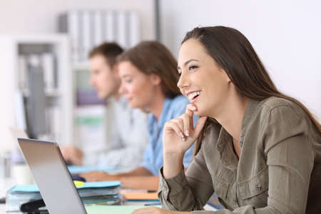 Portrait of a happy employee imagining sitting in a desktop at officeの写真素材