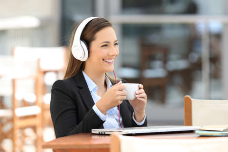 Single executive listening audio content and holding a cup sitting in a coffee shopの写真素材