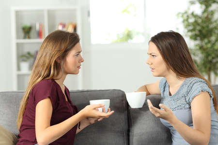 Two friends talking seriously sitting on a couch at homeの写真素材