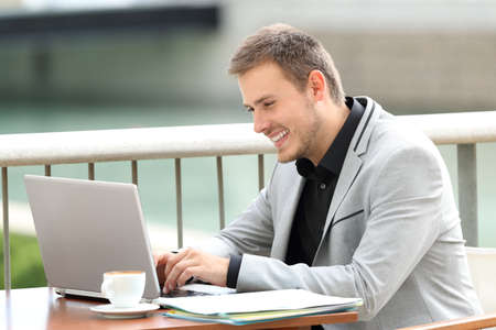 Happy executive man typing in a laptop sitting in a coffee shopの写真素材