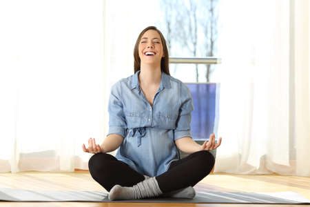 Front view portrait of a happy pregnant woman practicing yoga exercises on the floor at homeの写真素材