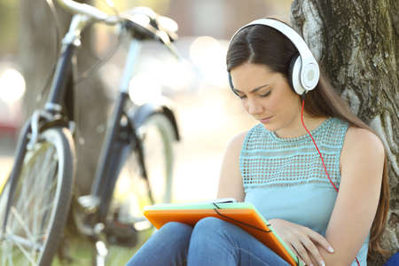 Single student wearing headphones learning hearing audio tutorials sitting in a parkの写真素材