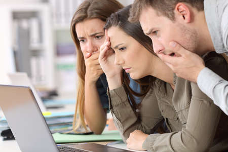 Three worried employees reading bad news on line in a laptop at officeの写真素材