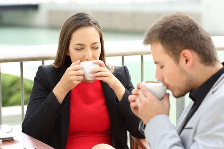 Two happy executives drinking coffee cups sitting in a bar terraceの写真素材