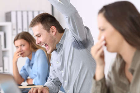 Man showing a sweaty and stinky underarm and disgusted colleagues at officeの写真素材