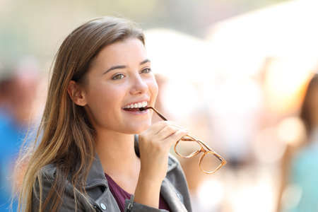 Portrait of a happy beautiful girl biting eyeglasses on the streetの写真素材