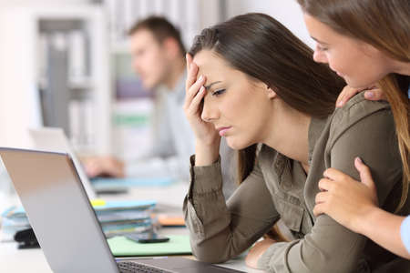 Sad employee receiving bad news on line being comforted by a colleague at office