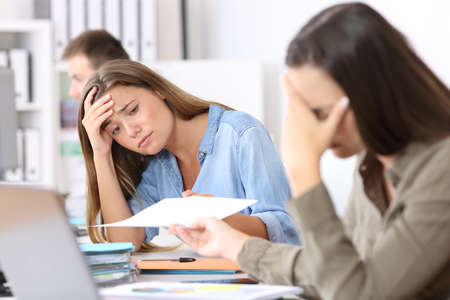 Portrait of two worried employees receiving bad news in a paper document at officeの写真素材