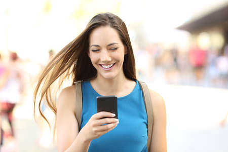 Front view portrait of a happy woman texting on the phone walking on the streetの写真素材