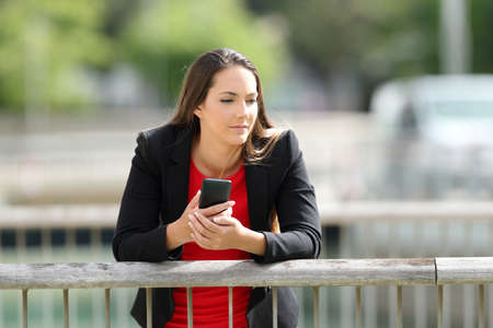 Pensive executive holding a mobile phone leaning in a railing outdoorsの写真素材