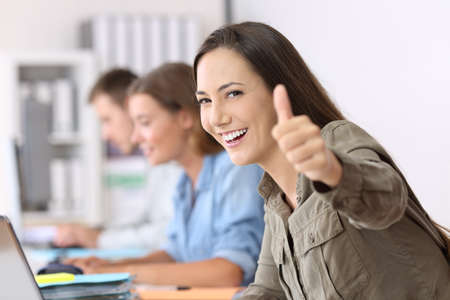 Portrait of a proud worker with thumbs up sitting in a desk at officeの写真素材