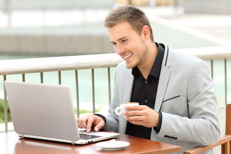 Smiley executive working on line with a laptop and holding a cup sitting in a coffee shopの写真素材