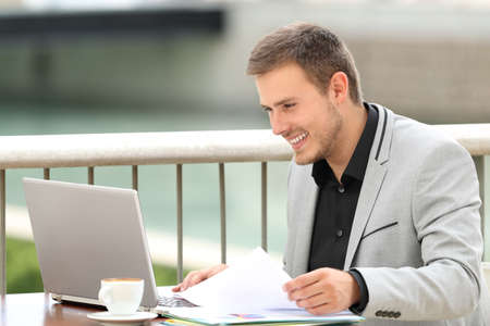 Single happy executive consulting on line content in a laptop sitting in a coffee shopの写真素材