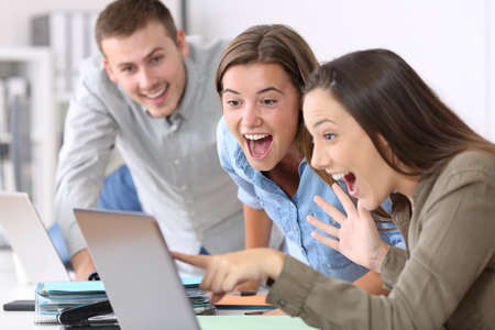 Three excited employees receiving good news on line at officeの写真素材