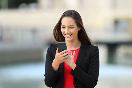 Happy executive walking and using phone outdoors in the streetの写真素材
