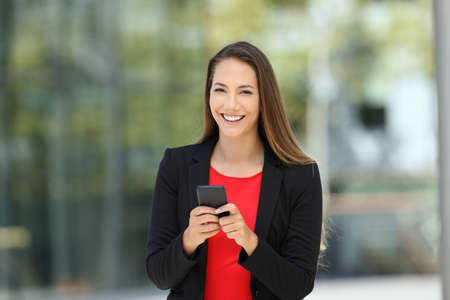 Single happy executive wearing suit and holding phone looking at you on the streetの写真素材