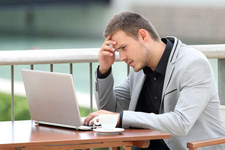 Single worried businessman reading bad news on line with a laptop sitting in a barの写真素材