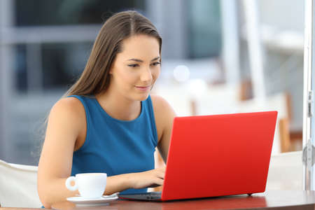 Single serious woman typing in a red laptop sitting in a barの写真素材