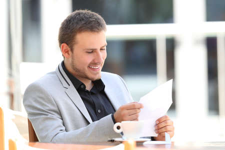 Single happy executive reading a letter sitting in a barの写真素材