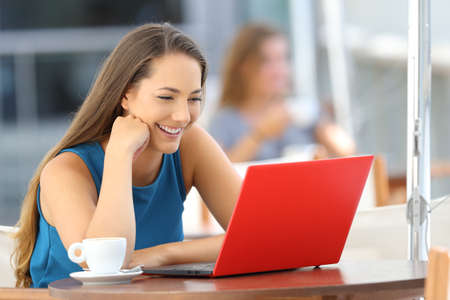 Single happy woman watching media content in a red laptop sitting in a restaurantの写真素材