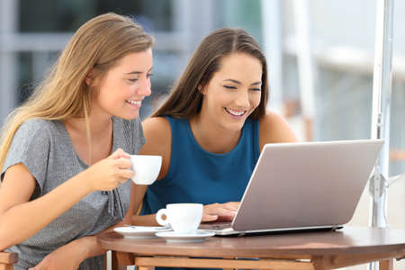 Two funny friends watching media content in a laptop sitting in a barの写真素材
