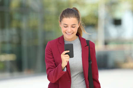 Front view portrait of a single executive reading phone messages and walking towards camera on the streetの写真素材