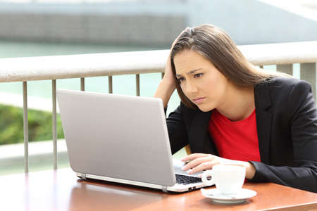 Single sad executive woman reading bad news on line in a laptop sitting in a coffee shopの写真素材