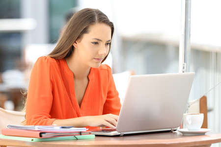 Single serious college student in orange using a laptop sitting in a coffee shopの写真素材