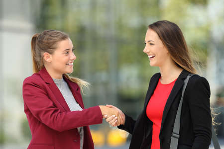 Side view of two happy executives meeting and handshaking on the street