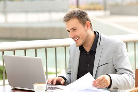 Single smiley executive working on line with a laptop sitting in a coffee shopの写真素材