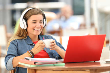 Single relaxed student watching media content in a red laptop sitting in a restaurantの写真素材
