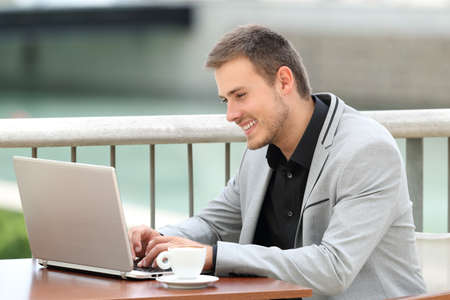 Happy executive writing in a laptop sitting in a bar outdoorsの写真素材
