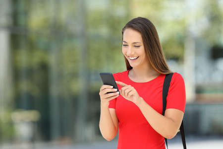 Single entrepreneur wearing a red dress using a mobile phone standing on the streetの写真素材