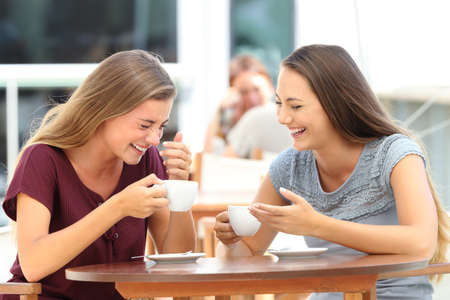 Two best friends laughing loud during a conversation sitting in a restaurantの写真素材