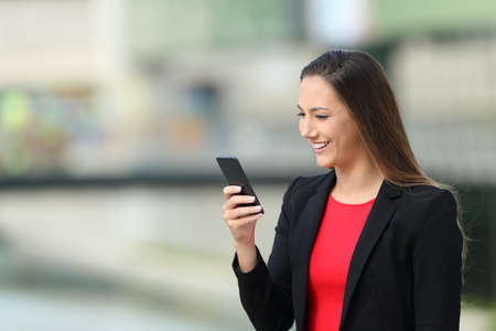 Single happy executive girl reading messages on phone walking on the streetの写真素材