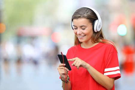 Single happy teen in red listening to music on line with phone and headphones walking on the streetの写真素材