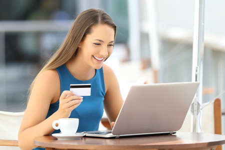 Single happy woman paying on line with a credit card and a laptop in a restaurantの写真素材
